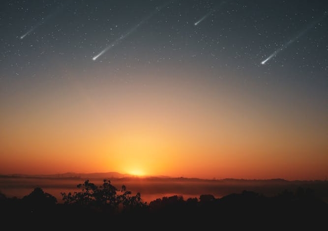 Experience the awe-inspiring beauty of a sunrise with shooting stars across a clear sky, perfect for serene landscapes.