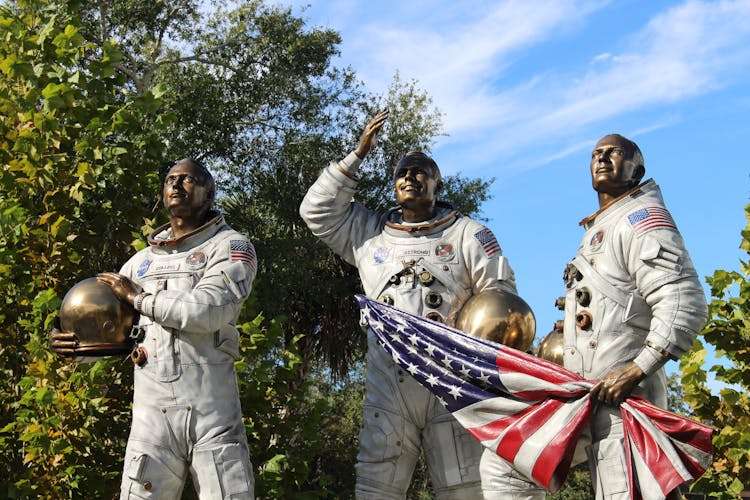 Bronze statue of Apollo astronauts at Cape Canaveral, holding a flag.